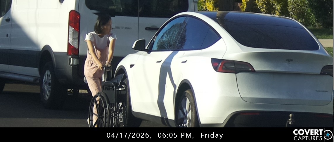 Woman with a blurred face holding a wheelchair beside a white car