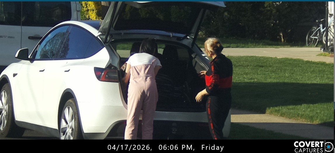Woman leaning toward a wheelchair in the open cargo area of a white car while another woman stands nearby