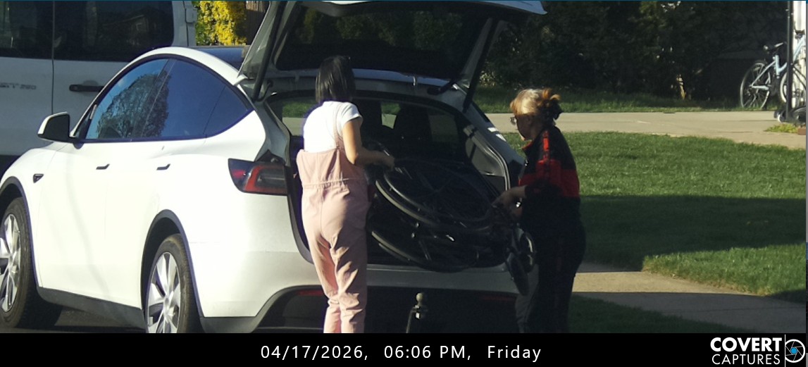 Woman holding a folded wheelchair at the open rear hatch of a white car, with another woman beside the vehicle