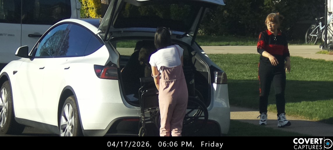 Woman handling a wheelchair directly behind the rear bumper of a white car