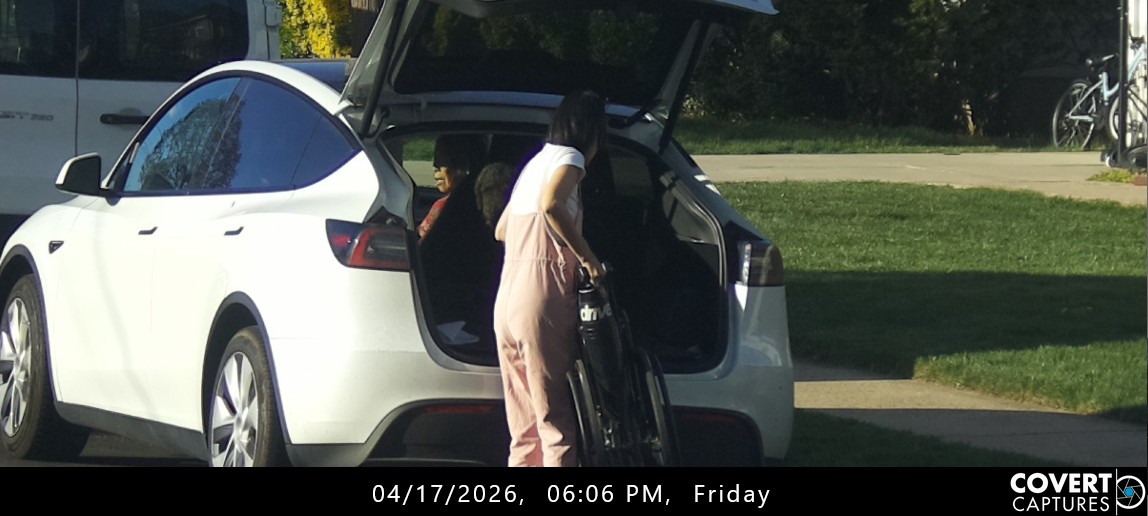 Woman holding a folded wheelchair beside the open rear hatch of a white car