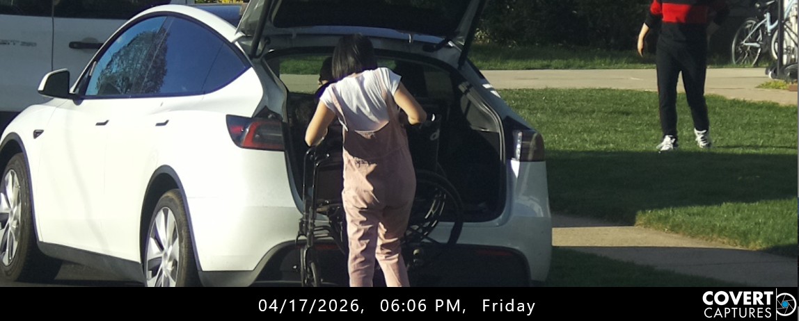 Rear view of a woman handling a wheelchair beside the open cargo area of a white car